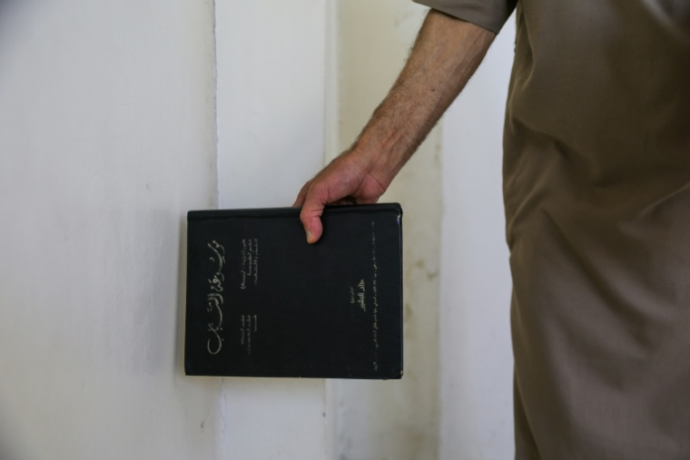 Mustafa Khaled Alwan tient un livre près de l'emplacement du faux mur qui dissimulait sa bibliothèque, chez lui à Homs, en Syrie, le 19 septembre 2026 ( AFP / Bakr ALKASEM )