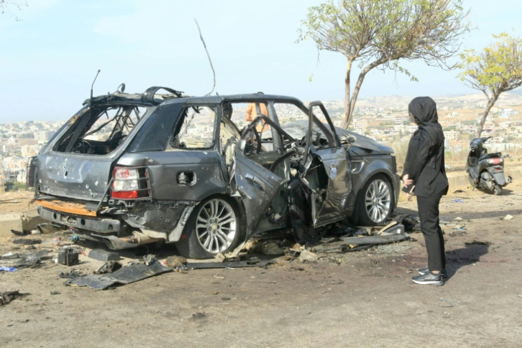 Une femme regarde le 2 novembre 2025 la carcasse d'une voiture, visée la veille par une frappe israélienne ayant tué ses occupants, dans dans le sud du Liban dans le district de Nabatiyeh ( AFP / Mahmoud ZAYYAT )