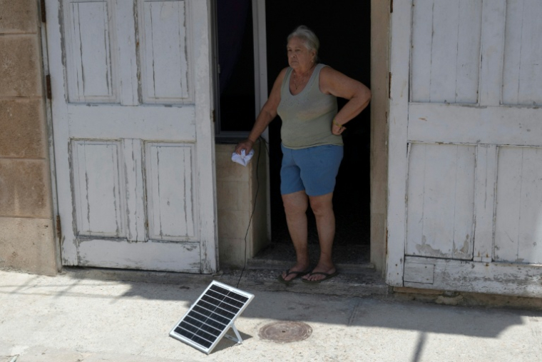 Une habitante sur le seuil de sa maison près d'un panneau solaire, le 6 juillet 2026 à La Havane, lors d'une panne de courant nationale à Cuba ( AFP / YAMIL LAGE )