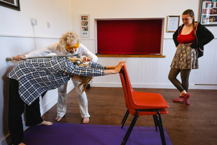 Dorothea Barron, 100 ans, vétérane britannique de la Seconde Guerre mondiale, aide une élève à étirer son dos lors d'un cours de yoga près de Harlow, le 31 mars 2025 au nord de Londres ( AFP / Adrian DENNIS )