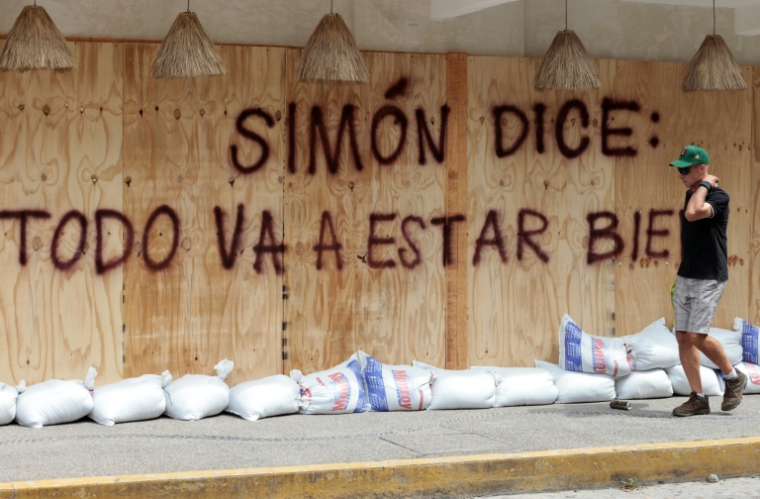 Un homme passe devant un message: "Simon a dit: +tout va bien se passer+", peint sur des planches de protection en prévision de l'arrivée du cyclone Simon à Puerto Vallarta au Mexique, le 10 octobre 2026 ( AFP / ULISES RUIZ )
