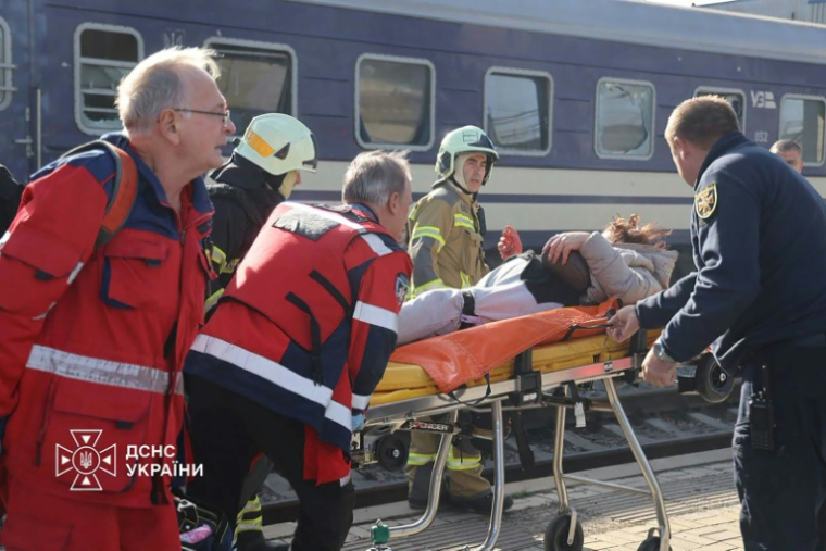 Photo diffusée par le Service ukrainien des situations d'urgence le 29 octobre 2026 montrant des secouristes ukrainiens transportant sur une civière une personne blessée après une attaque aérienne contre la gare de Dnipro, en Ukraine ( UKRAINIAN EMERGENCY SERVICE / Handout )
