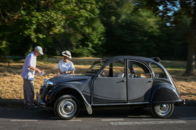 Des participants au 19ème défilé de voitures de collection de Paris à côté de leur 2CV le 19 juillet 2026 à Paris ( AFP / Lou BENOIST )