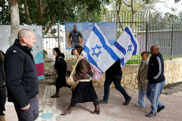 Des personnes portant des drapeaux israéliens se dirigent vers les funérailles de l'otage Ran Gvili, à Meitar, le 28 janvier 2026 ( AFP / John Wessels )