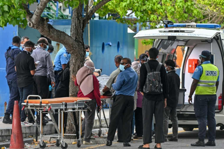 Des secouristes et des policiers transfèrent les corps de plongeurs italiens d'un bateau de la police à une ambulance, le 19 mai 2026 à Malé, aux Maldives ( AFP / Mohamed Afrah )
