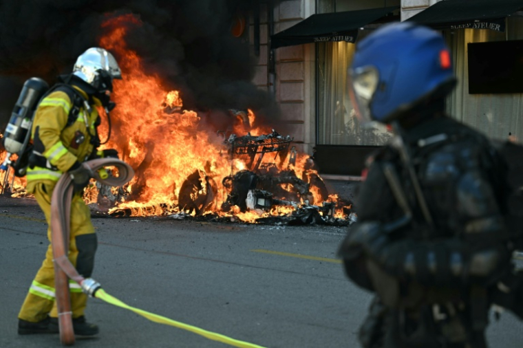 Un pompier tente d'éteindre une voiture Tesla incendiée lors d'une manifestation de la coalition "Non au G7", le 14 juin 2026 à Genève, en Suisse, à la veille du début du sommet du G7 à Evian, en France ( AFP / Fabrice COFFRINI )