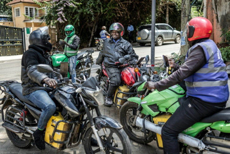 Des conducteurs de mototaxi, communément appelés "boda boda" en Afrique de l'Est, discutent assis sur leurs motos électriques en attendant des clients, le 21 mai 2026 à Nairobi, au Kenya ( AFP / Luis TATO )
