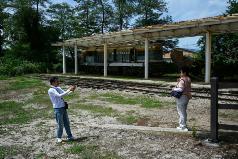 Des gens se prennent en photo devant une locomotive dans la gare de Woljeong-ri, dans la ville sud-coréenne de Cheorwon, près de la zone démilitarisée séparant les deux Corée, le 10 août 2026  ( AFP / GREG BAKER )