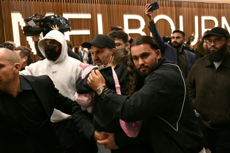 Un enfant australien revenant des camps de réfugiés syriens où il séjournait depuis la chute de l'Etat islamique est porté à travers une foule de journalistes à son arrivée à l'aéroport de Melbourne, le 7 mai 2026 ( AFP / WILLIAM WEST )