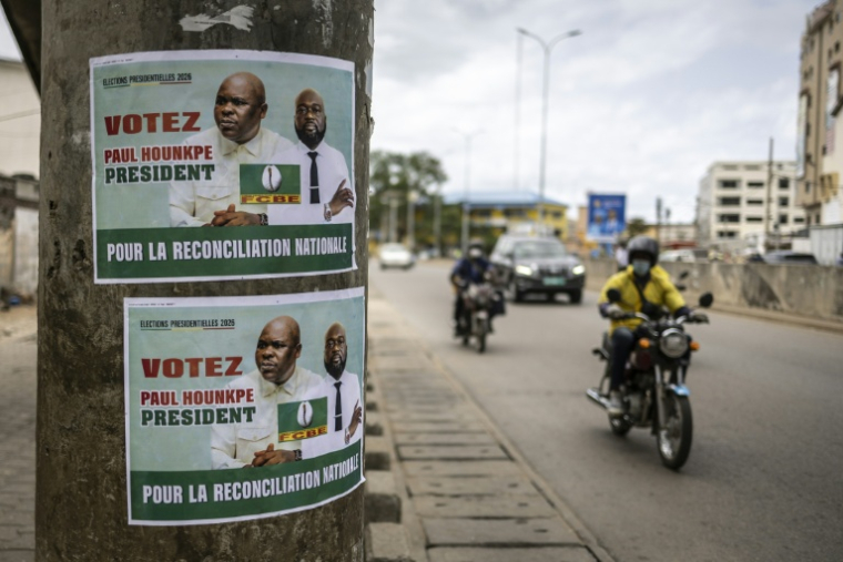 Des habitants de la capitale béninoise circulent à moto et en voiture près d'une affiche électorale, le 9 avril 2026 à Cotonou ( AFP / OLYMPIA DE MAISMONT )