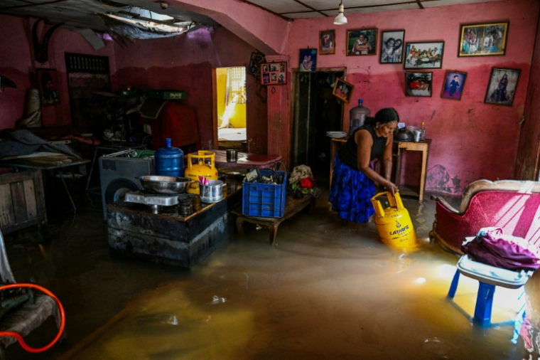 Une résidente transporte une bouteille de gaz liquéfié, dans une maison inondée, à Wellampitiya, en périphérie de Colombo, le 3 décembre 2025 ( AFP / Ishara S. KODIKARA )