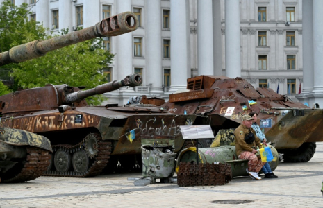 Un volontaire vend des drapeaux ukrainiens, assis sur les débris d'un missile, à Kiev, le 19 mai 2025 ( AFP / Sergei SUPINSKY )