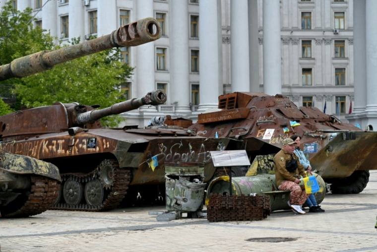 Un volontaire vend des drapeaux ukrainiens, assis sur les débris d'un missile, à Kiev, le 19 mai 2025 ( AFP / Sergei SUPINSKY )