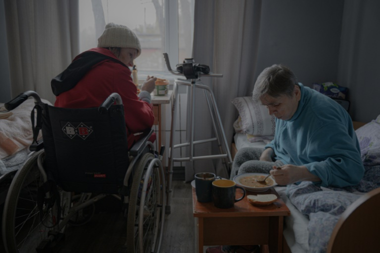 Deux femmes âgées prennent leur repas dans leur chambre, dans un refuge pour seniors à Kharkiv, en Ukraine, le 26 mars 2025 ( AFP / Ivan SAMOILOV )