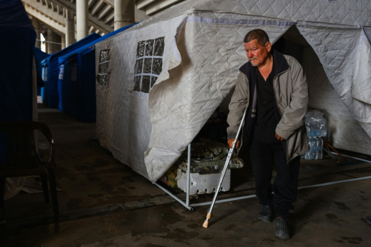 Un homme marche avec une béquille devant sa tente, dans le stade Camille Chamoun transformé en centre d'accueil et d'hébergement pour personnes déplacées, le 27 mars 2026 à Beyrouth, au Liban ( AFP / Dimitar DILKOFF )