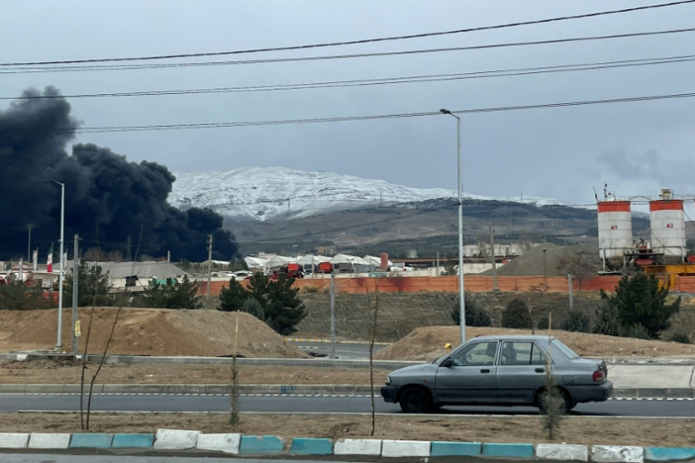 Des véhicules roulent sur une autoroute à proximité d'un épais nuage de fumée à Téhéran, cible de frappes aériennes israélo-américaines, le 8 mars 2026  ( AFP / - )