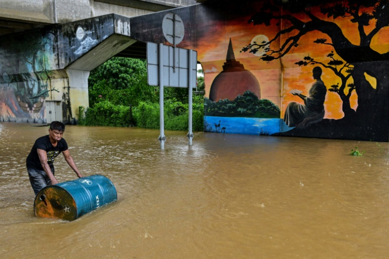 Un homme, portant ses affaires, traverse une route inondée après de fortes pluies à Kaduwela, dans la périphérie de Colombo, le 28 novembre 2025 ( AFP / Ishara S. KODIKARA )