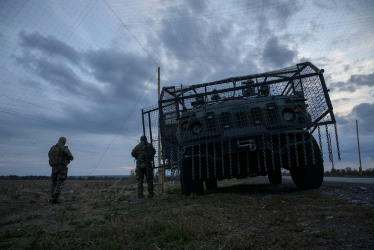 Des soldats ukrainiens devant un véhicule militaire blindé entouré d'une cage de protection contre les attaques de drones, sur une route près d'Oleksandrivka, le 6 octobre 2025 ( AFP / Ed JONES )