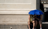 Des personnes utilisent un parapluie pour s'abriter du soleil près de la Pyramide du Louvre lors d'une vague de chaleur, à Paris, le 26 juin 2019 ( AFP / Kenzo TRIBOUILLARD )
