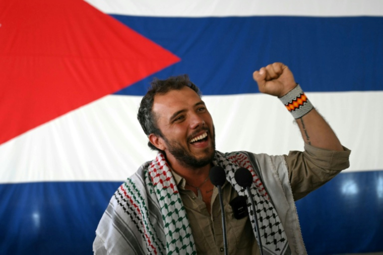 L'activiste brésilien Thiago Avila lève le poing et sourit devant un drapeau cubain après son arrivée au port de La Havane à bord du bateau de pêche Maguro, faisant partie de la flottille d'aide humanitaire, le 24 mars 2026  ( AFP / Yuri Cortez )