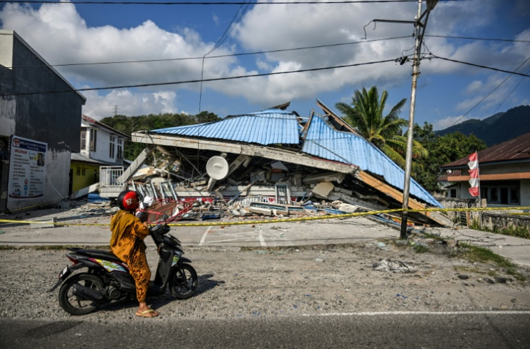 Une moto s'arrête le 16 août près d'un bâtiment effondré à la suite d'un séisme de magnitude 7,7 qui a secoué samedi l'île de Florès, en Indonésie ( AFP / JUNI KRISWANTO )
