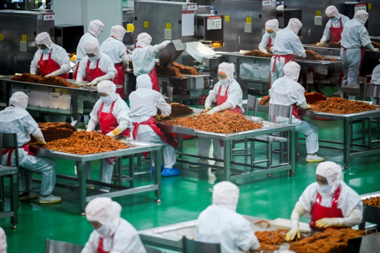 Des ouvriers préparent des lamelles de farine pour les aromatiser avant leur conditionnement à l'usine Mala Wangzi, du comté de Pingjiang, dans la province du Hunan, le 17 juin 2026 dans le centre de la Chine ( AFP / WANG Zhao )