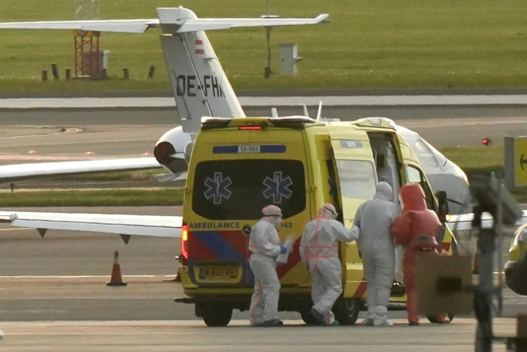 Une personne en combinaison de protection (2e d) escortée vers une ambulance depuis un avion médicalisé transportant des passagers du bateau de croisière MV Hondius, soupçonnés d'être infectés par le hantavirus, à l'aéroport de Schiphol, le 6 mai 2026 près d'Amsterdam, aux Pays-Bas ( AFP / Lina Selg )