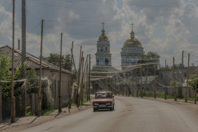 Une voiture circule sur une route recouverte de filets anti-drones, devant la cathédrale Sainte-Ascension, à Izioum, région de Kharkiv dans l'est de l'Ukraine, le 22 juillet 2026 ( AFP / Roman PILIPEY )