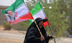 Une pèlerine iranienne brandit des drapeaux iraniens dont l'un comprend un portrait du guide suprême Ali Khamenei, tué dans un bombardement américain, le 29 juillet 2026 dans la ville-frontière de Zurbatiyah, en Irak ( AFP / AHMAD AL-RUBAYE )