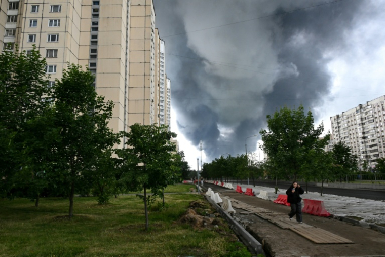 Une femme marche dans un quartier résidentiel tandis que de la fumée noire s'élève du site de la raffinerie russe de Gazprom Neft,  située dans la banlieue sud-est de Moscou, le 18 juin 2026. L'Ukraine a mené tot le 18 juin une attaque de drones "de grande envergure" contre Moscou, plusieurs d'entre eux ayant atteint une raffinerie de pétrole, a déclaré le maire de la ville, Sergueï Sobianine. ( AFP / - )