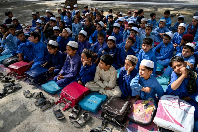 Des écoliers portent des tuniques et chapeaux selon le nouveau code d'uniforme, lors d'une classe en extérieur, à Mohmand Dara, dans la province de Nangarhar, le 20 avril 2025 en Afghanistan ( AFP / Wakil KOHSAR )