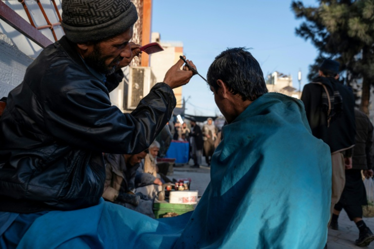 Un barbier coupe les cheveux d'un client dans une rue de Kaboul le 11 février 2026 ( AFP / Wakil KOHSAR )
