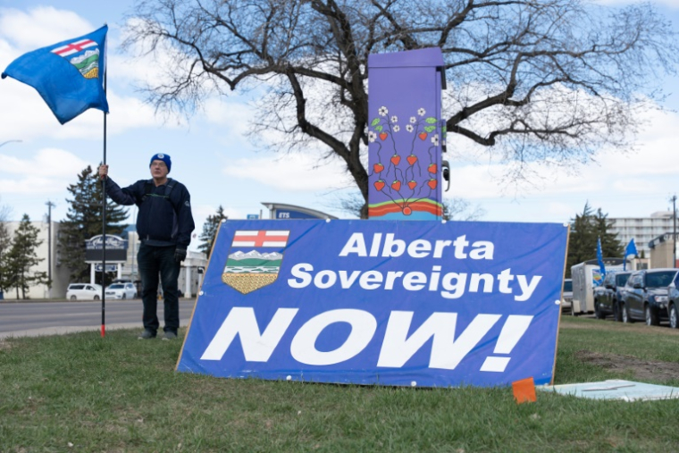Un partisan séparatiste tenant un drapeau, à côté d'une pancarte réclamant la souveraineté de la province de l'Alberta "maintenant", à Edmonton au Canada le 4 mai 2026. ( AFP / Henry MARKEN )