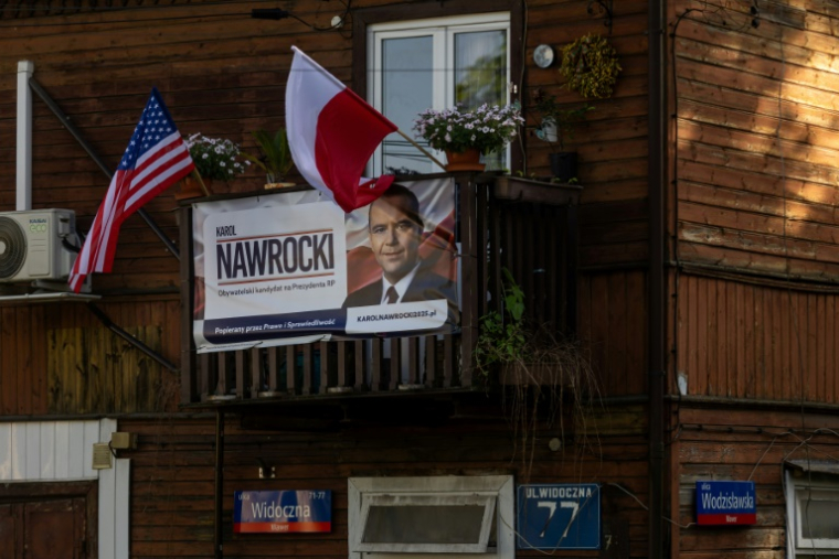 Une affiche électorale de Karol Nawrocki, candidat à l'élection présidentielle, soutenu par le parti de droite polonais Droit et Justice (PiS), exposée sur un balcon à côté des drapeaux polonais et américain, le 6 mai 2025 à Varsovie ( AFP / Wojtek RADWANSKI )