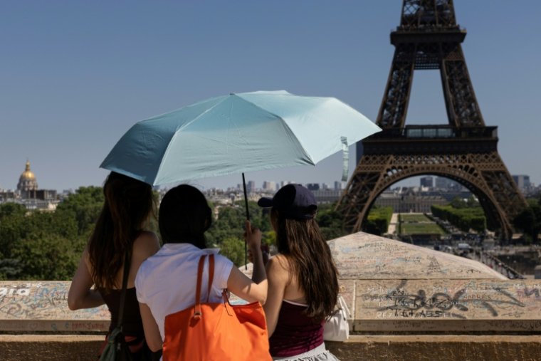Des touristes se protègent du soleil sous un paraplluie devant la Tour Eiffel lors d'une vague de chaleur à Paris, le 27 mai 2026 ( AFP / JOEL SAGET )