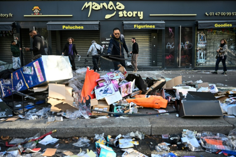 Un commerçant déblaie les débris devant sa boutique endommagée, au lendemain de manifestations nationales contre la vie chère, le 18 octobre 2026 à Paris ( AFP / Matthieu RONDEL )