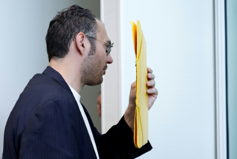David G., animateur périscolaire, se cache le visage avec un dossier à son arrivée au tribunal où il doit être jugé pour agressions sexuelles sur neuf enfants, le 26 mai 2026 ( AFP / SIMON WOHLFAHRT )