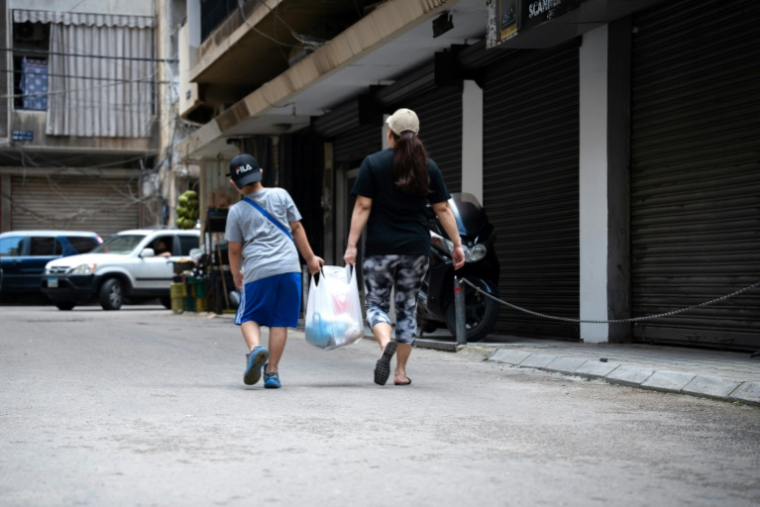 Une migrante et son fils chargés d'un sac de provsions quittent le centre de l'organisation caritative "Tres Marias" à Beyrouth, le 16 mai 2026 au Liban ( AFP / Chantale SALAMEH )