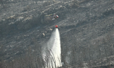 Un hélicoptère de la Sécurité civile déverse sa cargaison d'eau près du village de Coustouge, dans l'Aude touchée par des incendies, le 8 août 2025  ( AFP / Lionel BONAVENTURE )