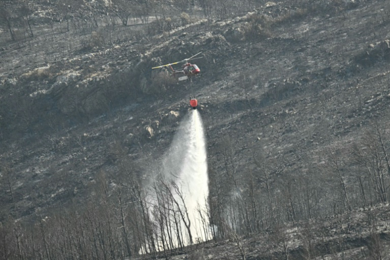 Un hélicoptère de la Sécurité civile déverse sa cargaison d'eau près du village de Coustouge, dans l'Aude touchée par des incendies, le 8 août 2025 ( AFP / Lionel BONAVENTURE )