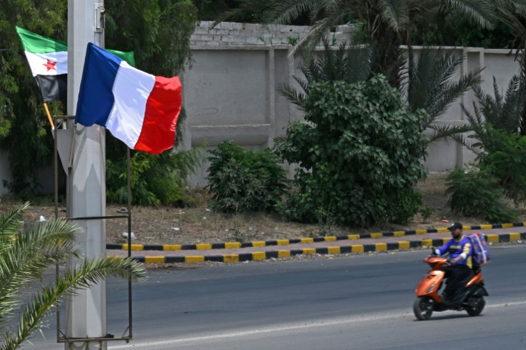 Un motocycliste passe devant des drapeaux syrien et français déployés le long de la route menant à l'aéroport, le 6 juillet 2026 à Damas avant une visite du président Emmanuel Macron ( AFP / LOUAI BESHARA )