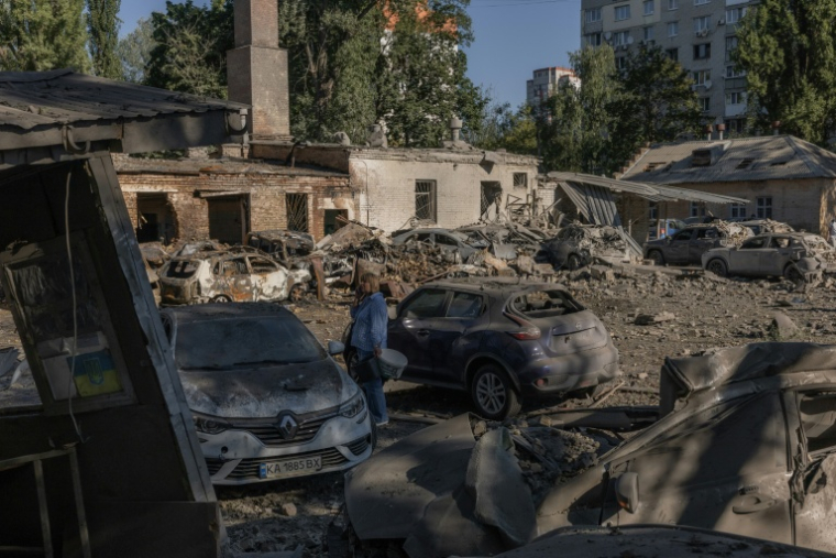 Une femme se tient près de voitures détruites et de bâtiments endommagés après une frappe russe à Kiev, le 20 août 2026 ( AFP / Roman PILIPEY )