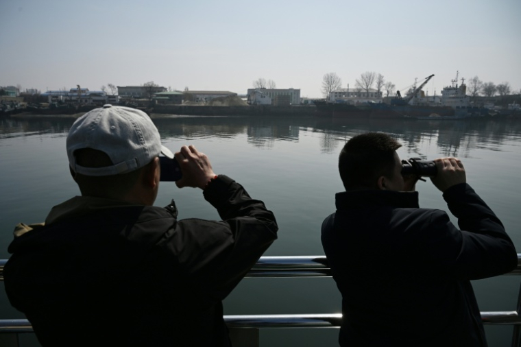 Des touristes observent la ville nord-coréenne de Sinuiju depuis un bateau touristique sur le fleuve Yalu, dans la ville frontalière de Dandong, dans le nord-est de la Chine, le 26 mars 2026 ( AFP / GREG BAKER )