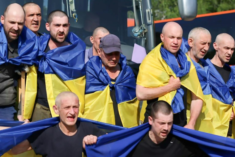 Photo diffusée par le Siège de coordination pour le traitement des prisonniers de guerre, le 10 juin 2025, des prisonniers de guerre ukrainiens, enveloppés de drapeaux nationaux, après un échange dans un lieu non divulgué ( Siège de coordination pour le traitement des prisonniers de guerre / Handout )