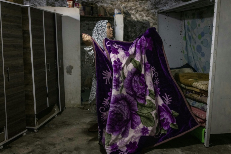 Arwa Amr plie une couverture en rangeant des placards précédemment détruits par les forces israéliennes, à l'intérieur des grottes que sa famille a transformées en foyer dans le village d'Al-Tuwani, en Cisjordanie occupée, le 11 septembre 2026 ( AFP / John WESSELS )