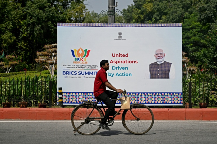 Un cycliste passe devant un panneau montrant le Premier ministre indien Narendra Modi, installé en amont du sommet des Brics, à New Delhi, le 9 septembre 2026 ( AFP / Sajjad HUSSAIN )