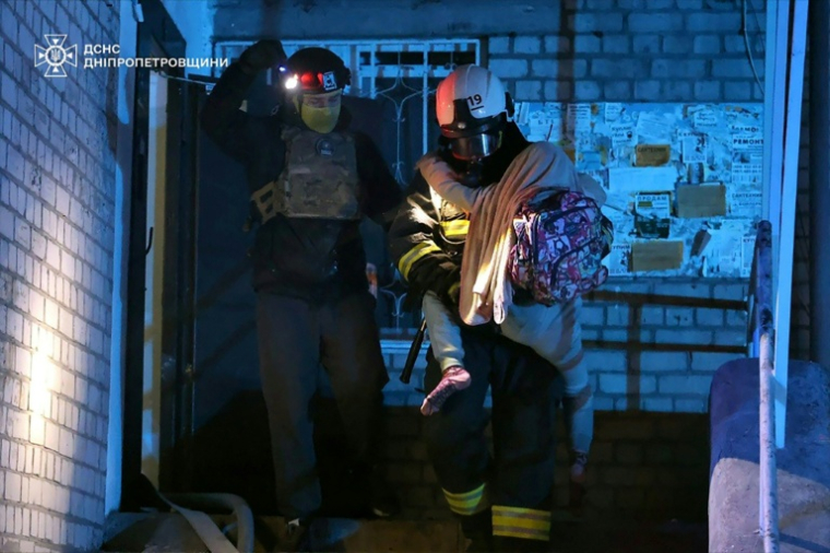 Photo prise et diffusée par le Service des situations d'urgence d'Ukraine, le 23 avril 2026, montrant des pompiers évacuant un enfant d'un immeuble résidentiel endommagé par une attaque russe à Dnipro ( Service des situations d'urgence d'Ukraine / Handout )