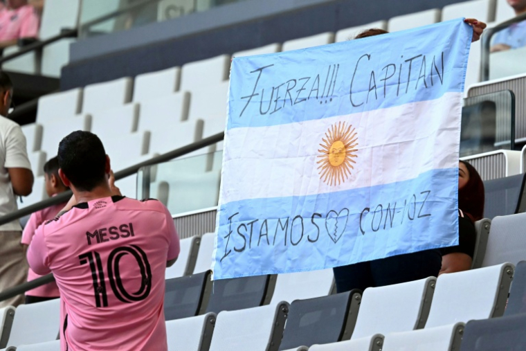 Un supporteur de l'Inter Miami tient un drapeau argentin portant un message de soutien pour Lionel Messi à la suite de la mort de son père, le 8 août 2026 à Miami ( AFP / CHANDAN KHANNA )