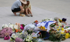 Des personnes se recueillent le 15 décembre 2025 devant des fleurs et un drapeau israélien déposés en mémoire des victimes d’une fusillade à Bondi Beach, à Sydney ( AFP / DAVID GRAY )