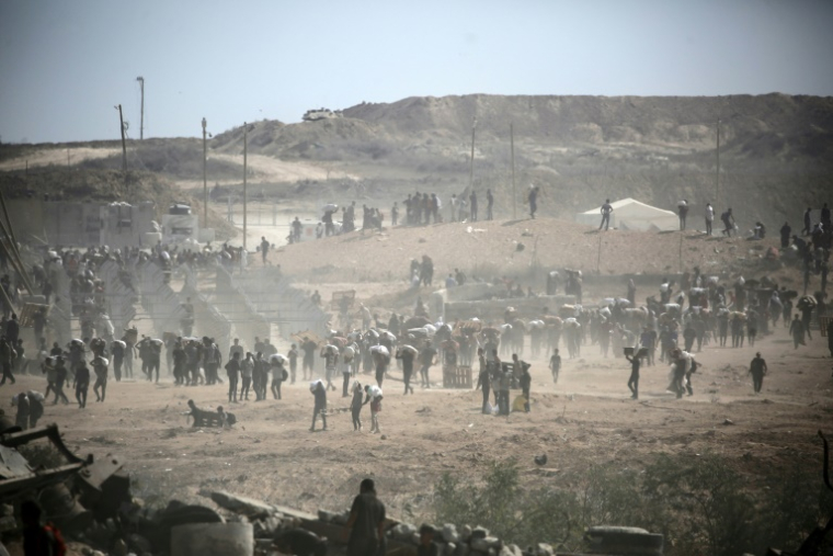Des Palestiniens portent des sacs d'aide près d'un point de distribution de nourriture, à Nousseirat dans le centre de la bande de Gaza, le 2 août 2025 ( AFP / Eyad BABA )